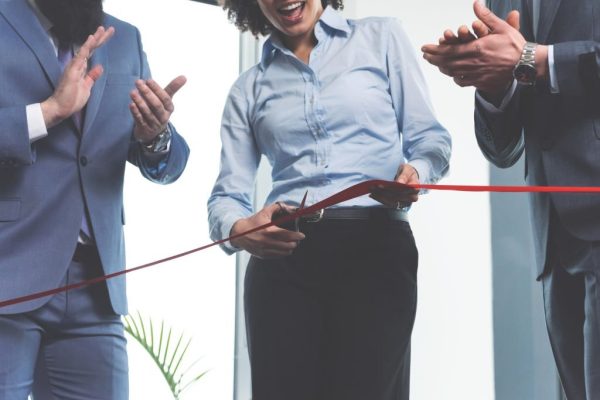 Team of ambitious young businesspeople on a ceremonial grand opening cutting red ribbon and clapping hands